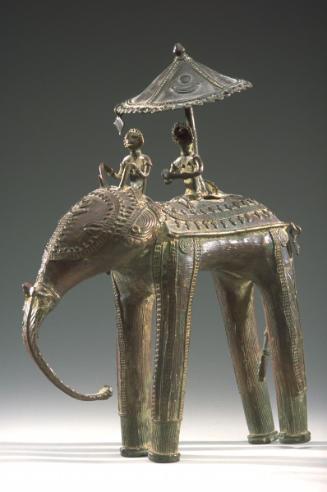 A figure under an parasol, on a mahout-driven elephant